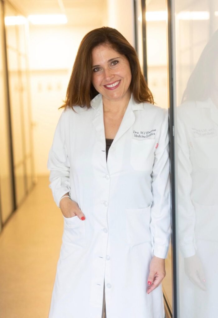 La Dra. María Jesús Huertas, médica estética, con bata blanca en un pasillo de la Clínica Avence de Murcia