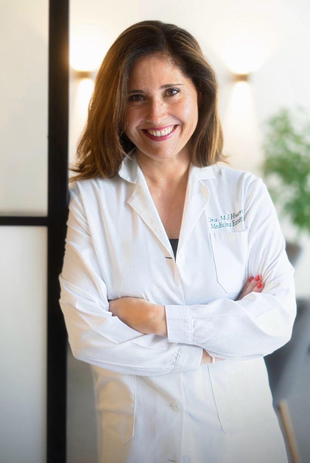 Retrato de la Dra. María Jesús Huertas con bata médica y los brazos cruzados, sonriendo